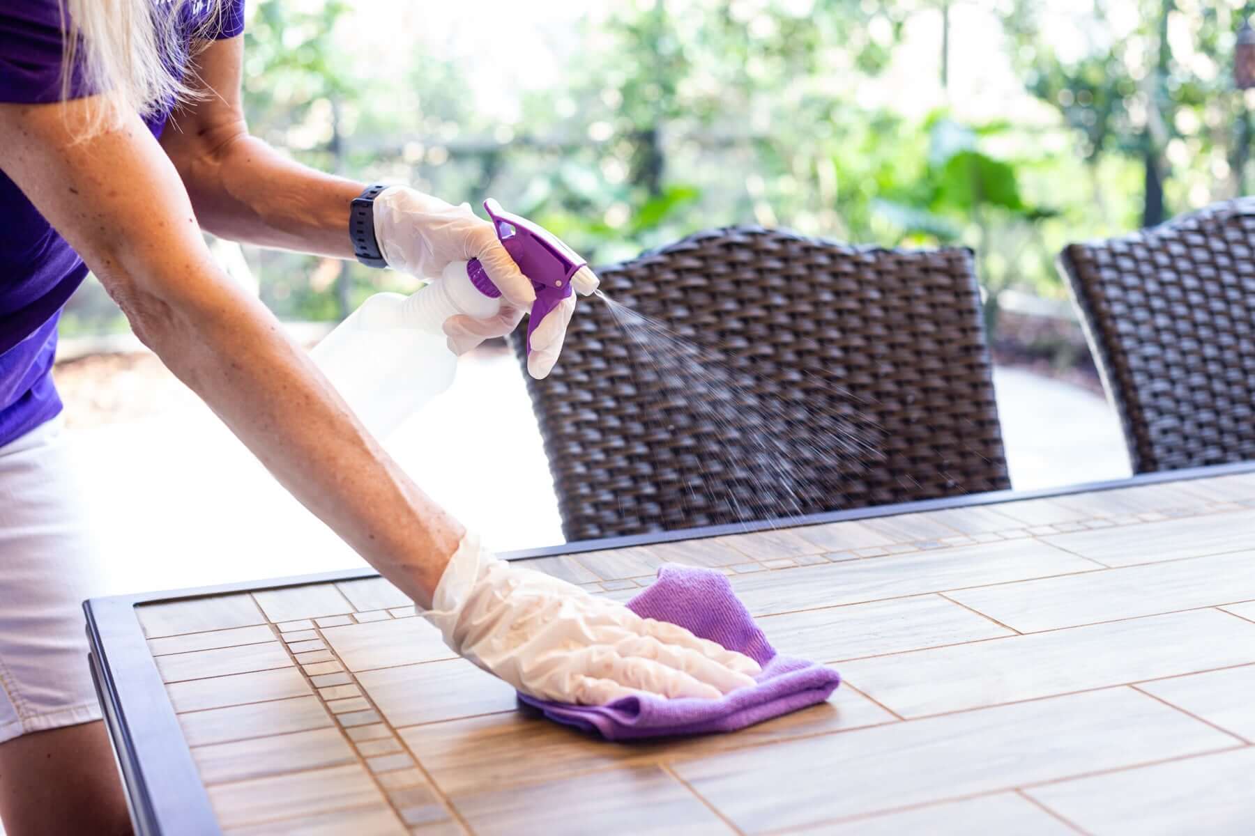 Maid in purple cleaning a table with spray and cloth, showcasing house cleaning services in Venice.